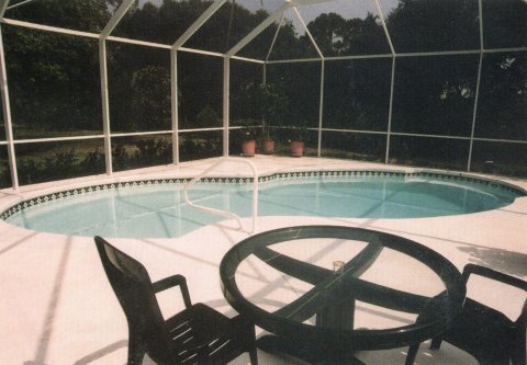 An enclosed pool with concrete decking and patio furniture.