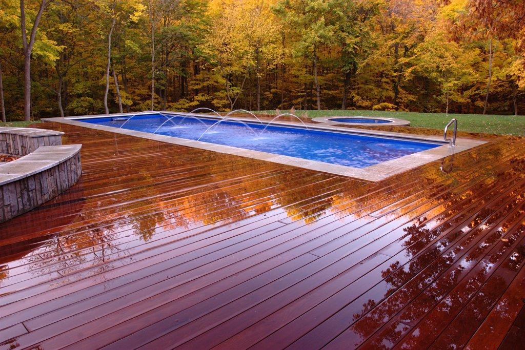 Enjoy a sun-soaked, pristine fiberglass pool in a tranquil backyard setting—perfect for relaxing and entertaining. Its sleek white borders and spacious wooden deck complement the lush greenery.