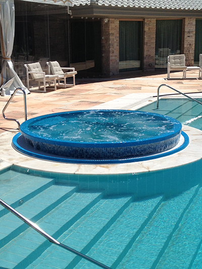 Elevate your backyard relaxation with this stunning fiberglass pool, featuring a central whirlpool for hydrotherapy and a serene glass-enclosed setting that captures the warm, golden light of a late-afternoon evening.