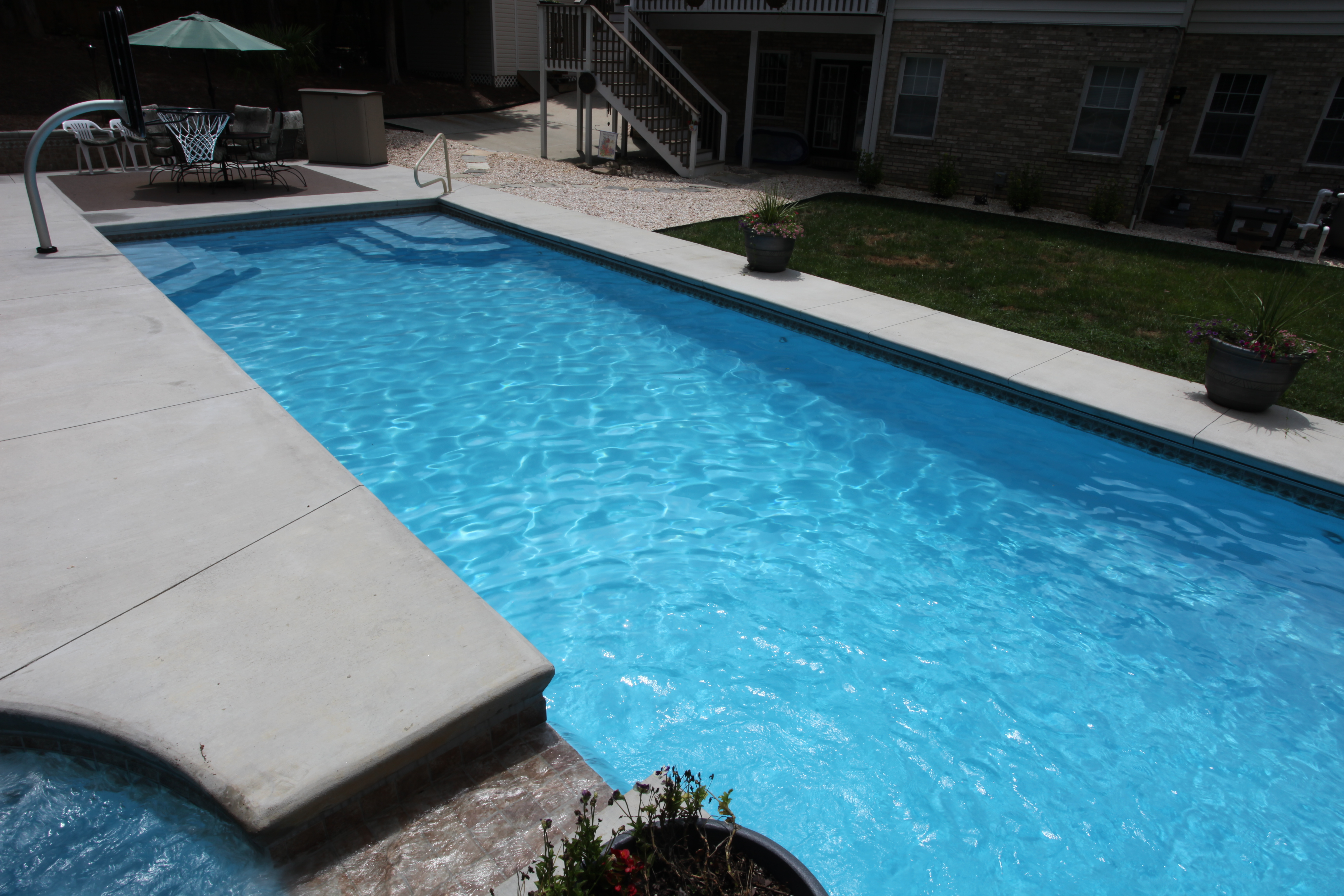 Experience the serene luxury of a freshly installed fiberglass inground pool, framed by a crisp white patio and lush green lawn for the perfect summer retreat.