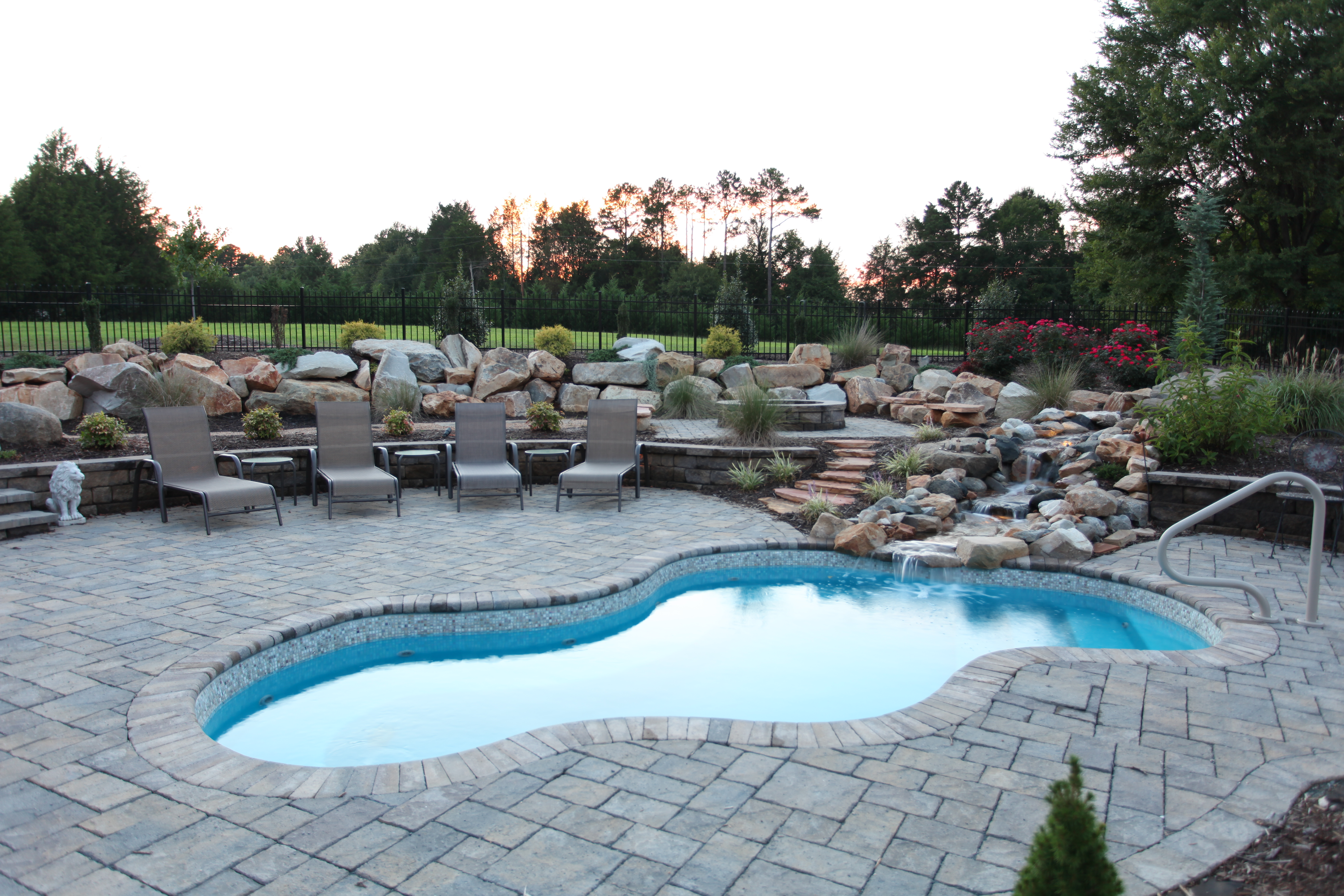 Enjoy this serene fiberglass pool in a lush backyard setting, featuring a kidney shape and natural stone surroundings.