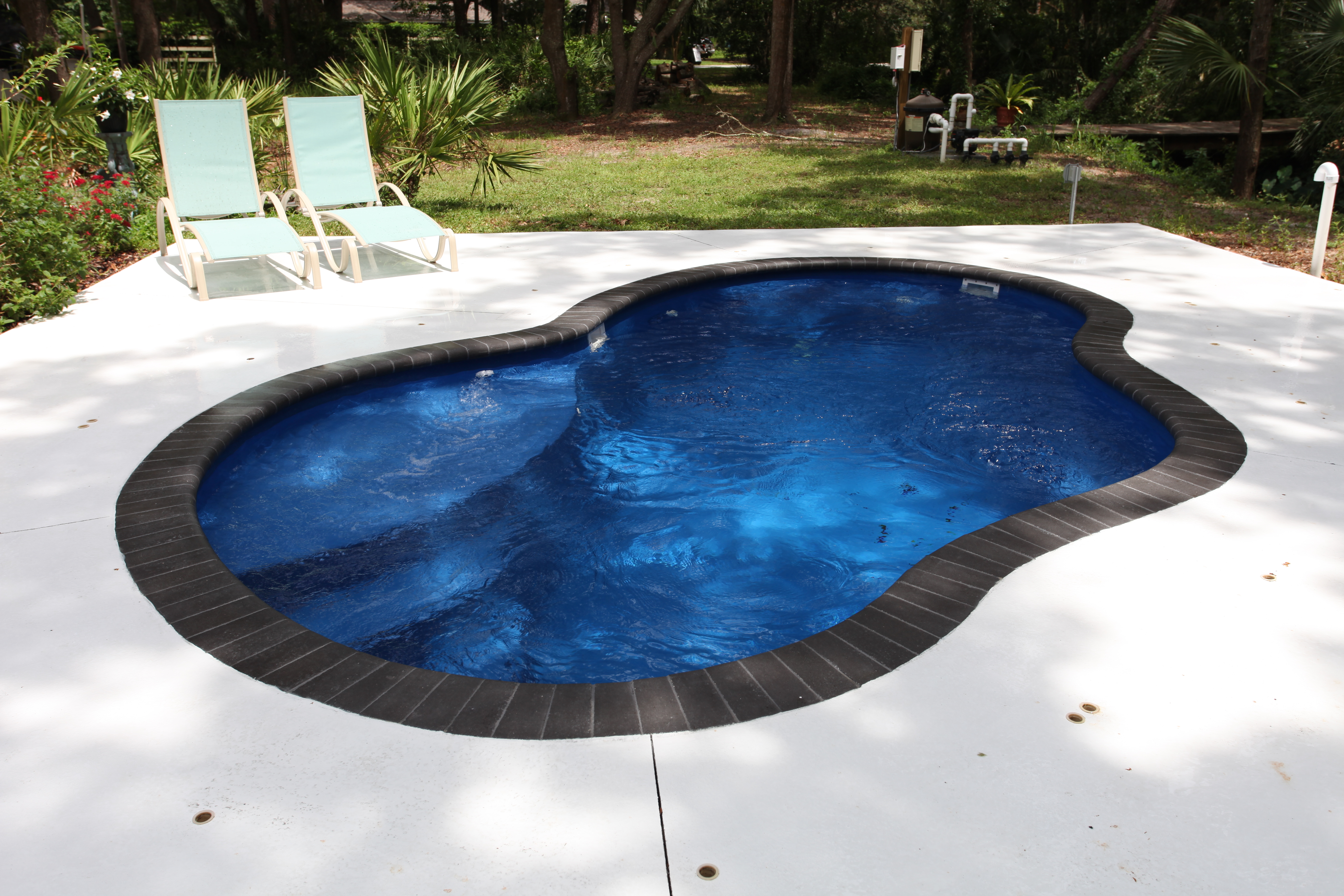 Experience tranquility with this serene fiberglass pool, featuring a kidney shape and dark blue liner, nestled in a lush coastal backyard.