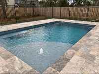 Fiberglass pool in a backyard with clear turquoise water and stone deck.
