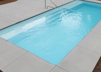 Rectangular fiberglass pool with clear turquoise water and tiled deck in a sunny backyard.