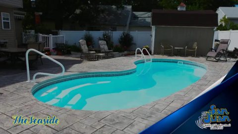 Finished fiberglass pool in a backyard with bright turquoise water and stone patio.