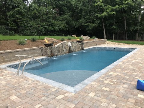 Fiberglass pool in a backyard with brick patio and stone wall.