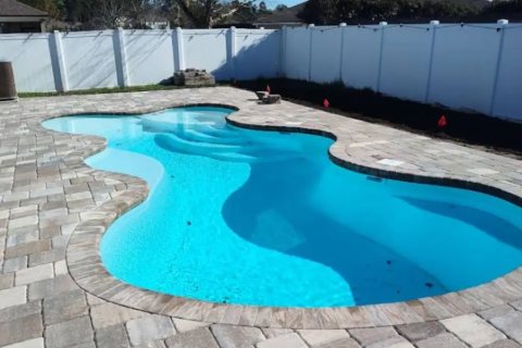 Finished fiberglass inground pool with turquoise water in a backyard patio