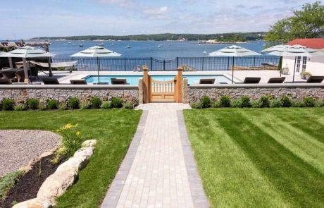 San Juan fiberglass pool in a lakeside backyard with stone wall and wooden gate